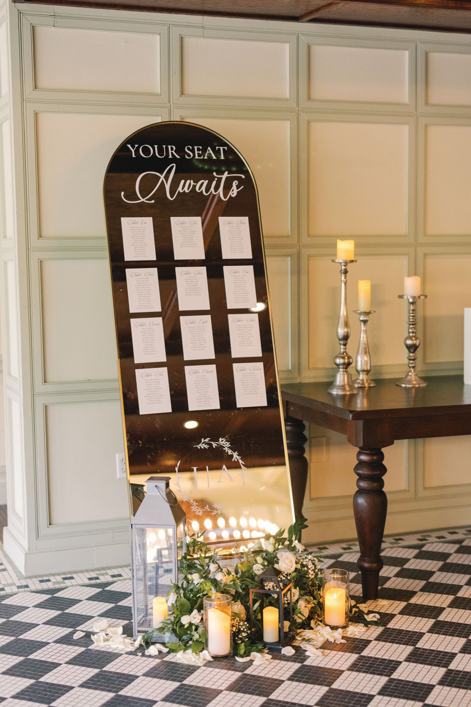 Elegant gold mirror seating chart display with candles and greenery at wedding reception.