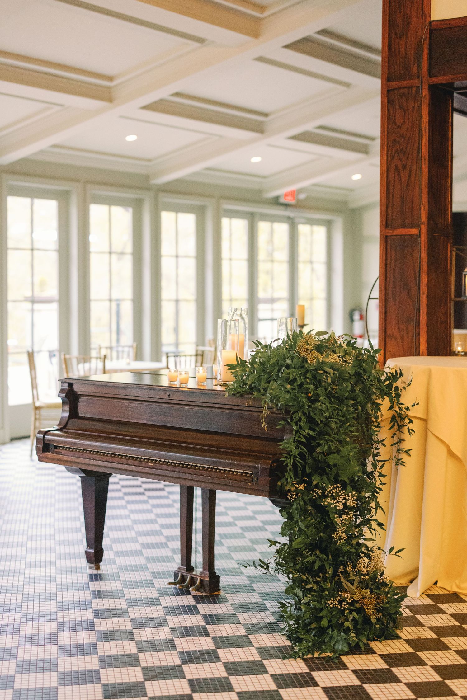 Vintage grand piano decorated with lush greenery garland in bright wedding venue interior.