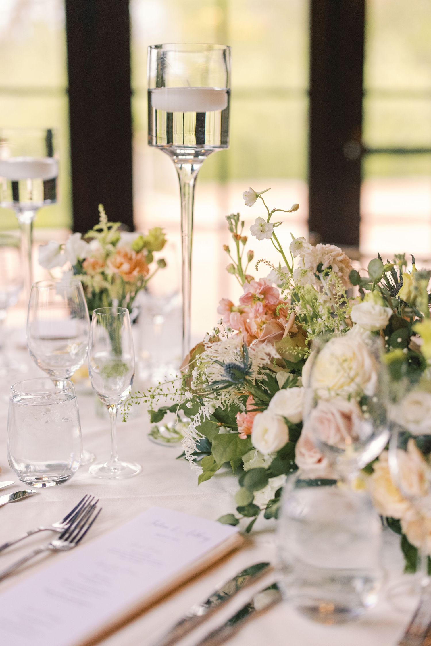 Elegant wedding reception table with blush floral centerpiece, tall glass candle holders, and fine dining settings.