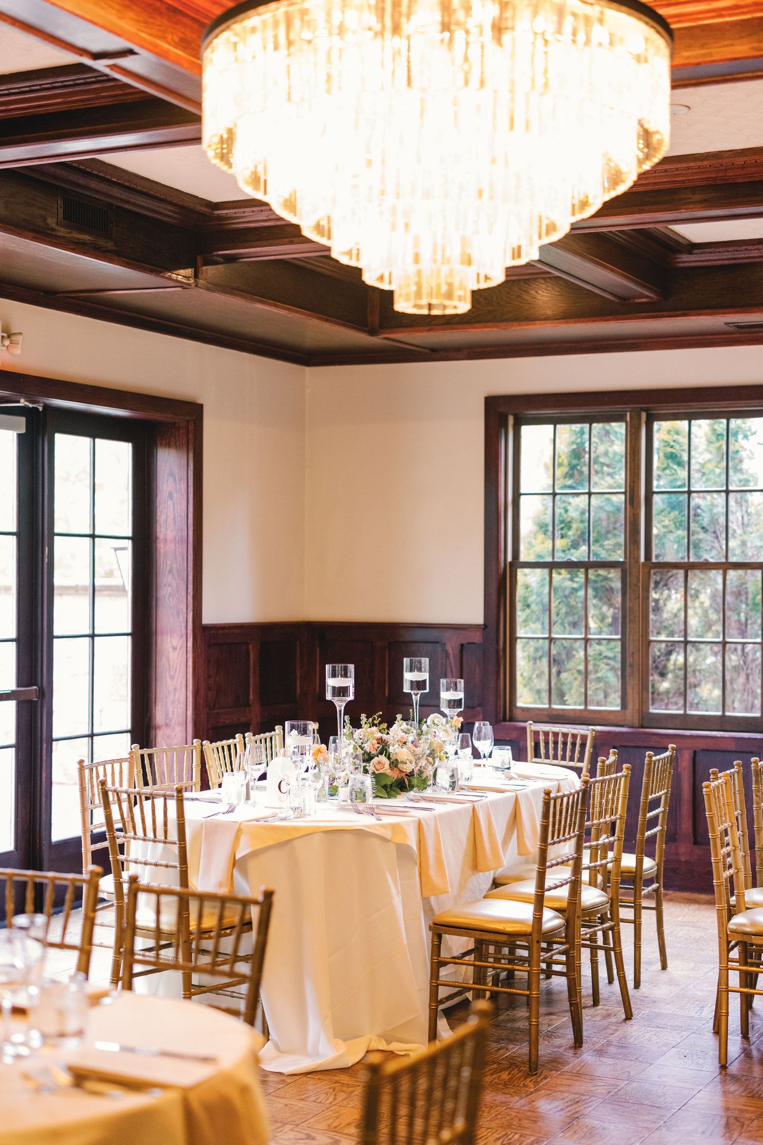 Classic wedding reception room with gold chiavari chairs, round tables, and a grand crystal chandelier.