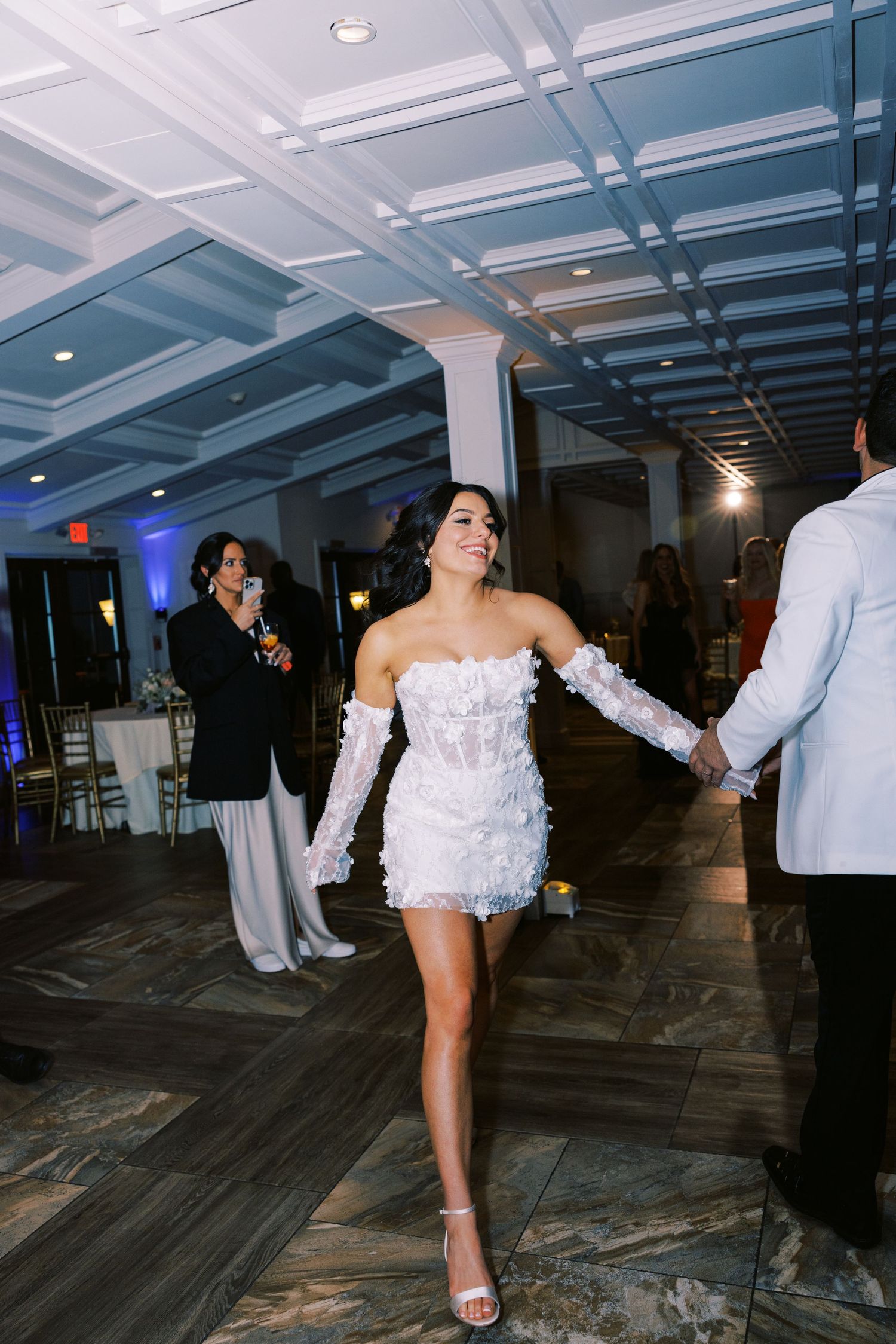 Bride in short white feathered reception dress with long gloves dancing at wedding reception.