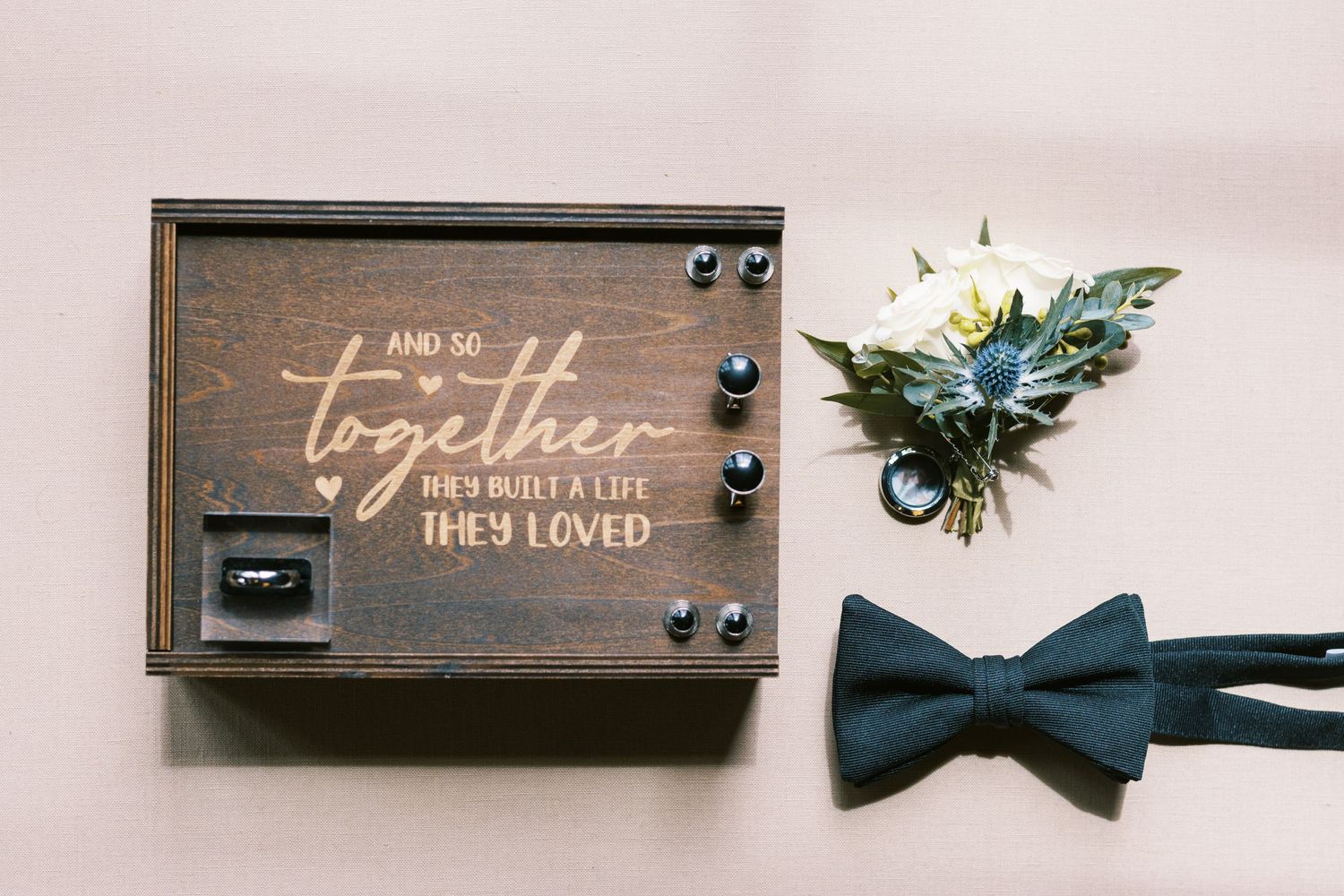 Wooden wedding ring box engraved with together quote displayed with navy bow tie and boutonniere.