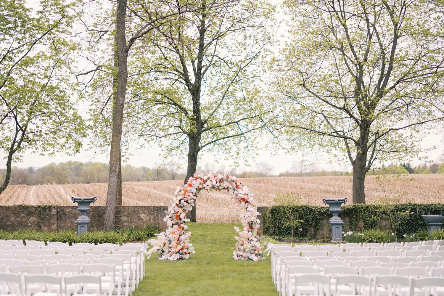 Elegant outdoor wedding ceremony setup with floral arch and white chairs on lush green lawn.
