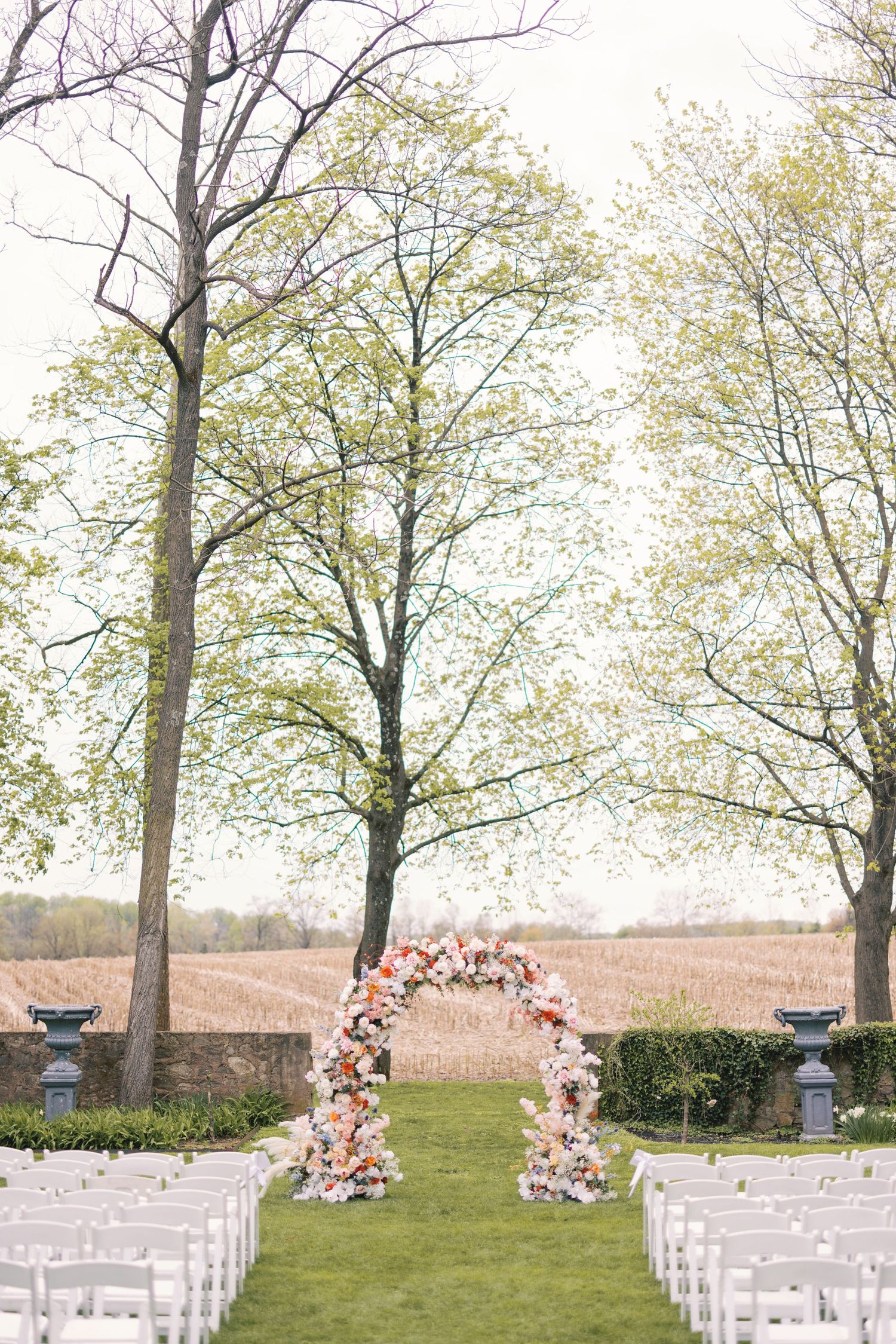 Romantic outdoor wedding ceremony with a stunning circular floral arch flanked by tall bare trees.