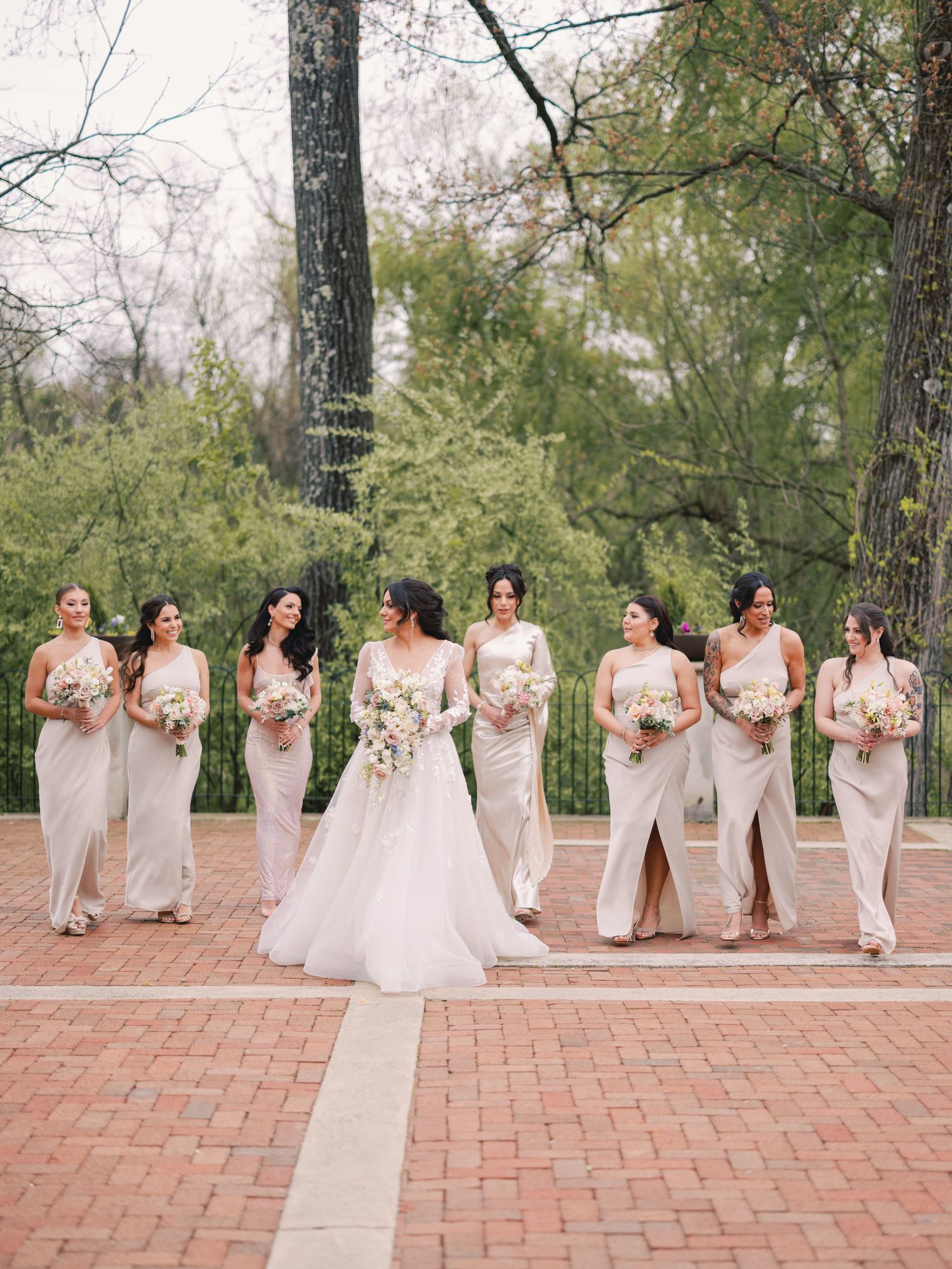 Bride in white ballgown walks with bridesmaids in champagne gowns carrying white floral bouquets.