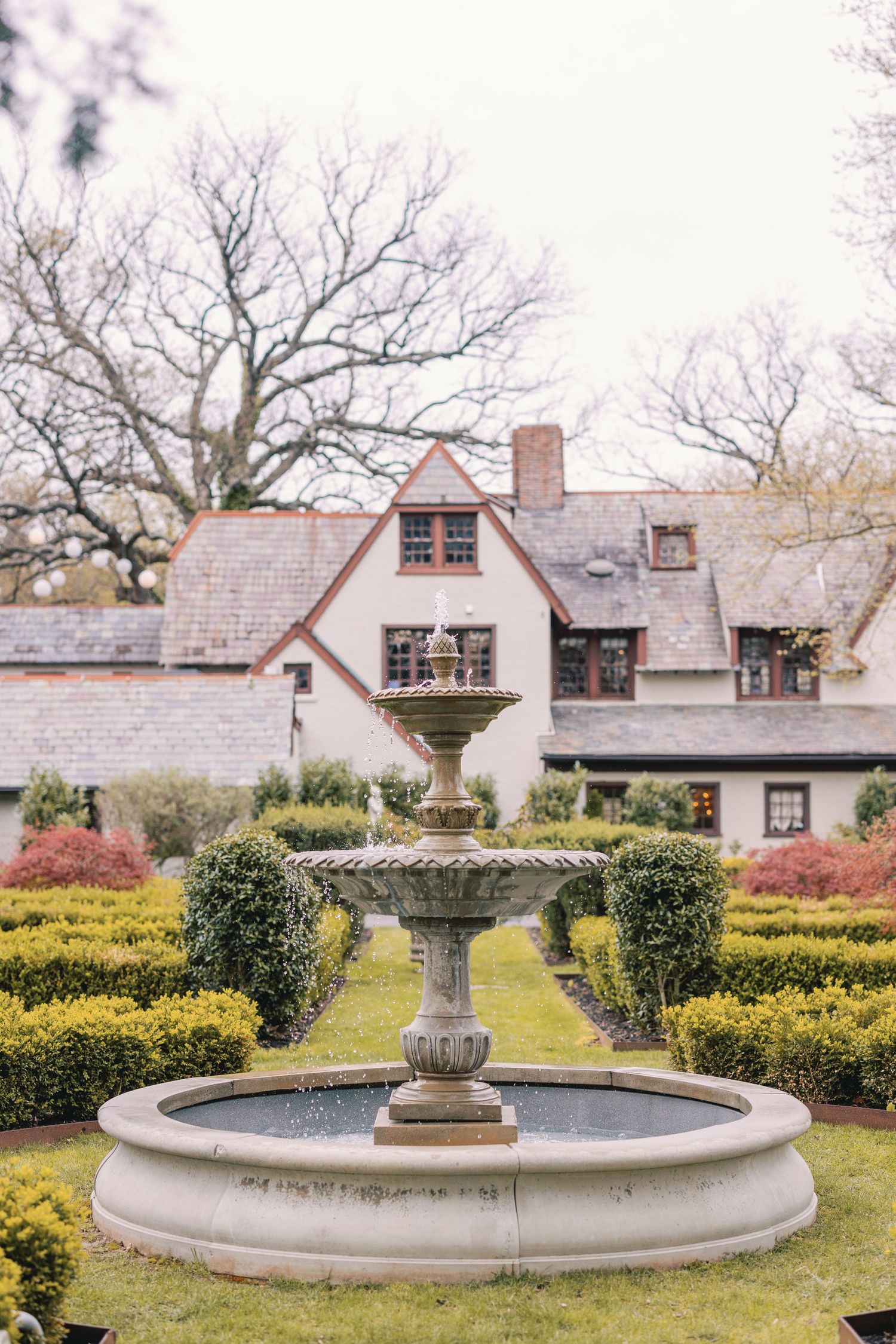 Elegant stone water fountain in manicured garden outside classic Tudor-style wedding venue estate.