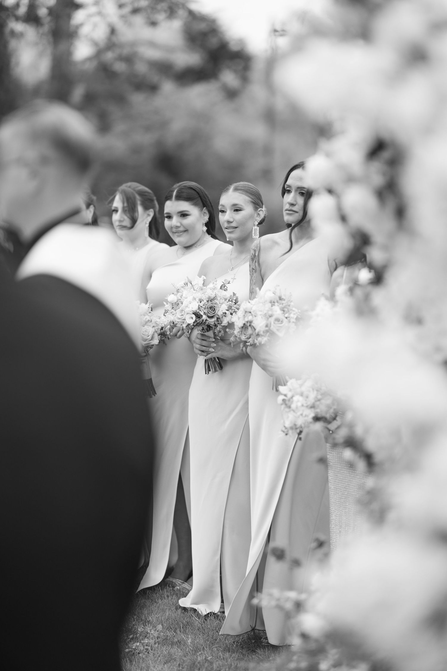 Black and white photo of bridesmaids holding bouquets during outdoor wedding ceremony.