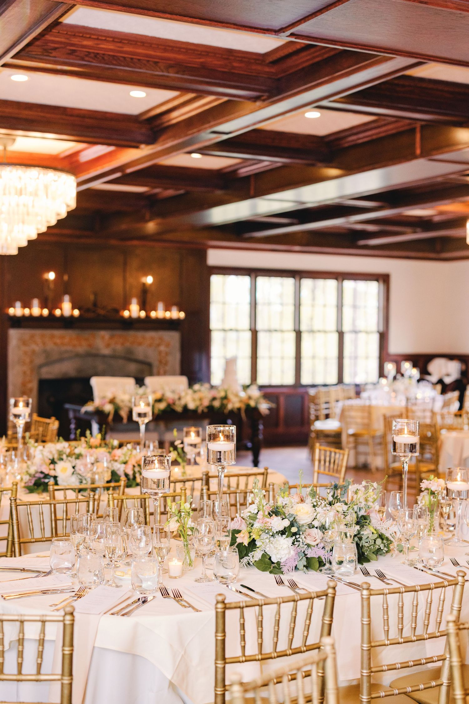 Elegant wedding reception hall with gold chiavari chairs, floral centerpieces, and chandelier lighting.