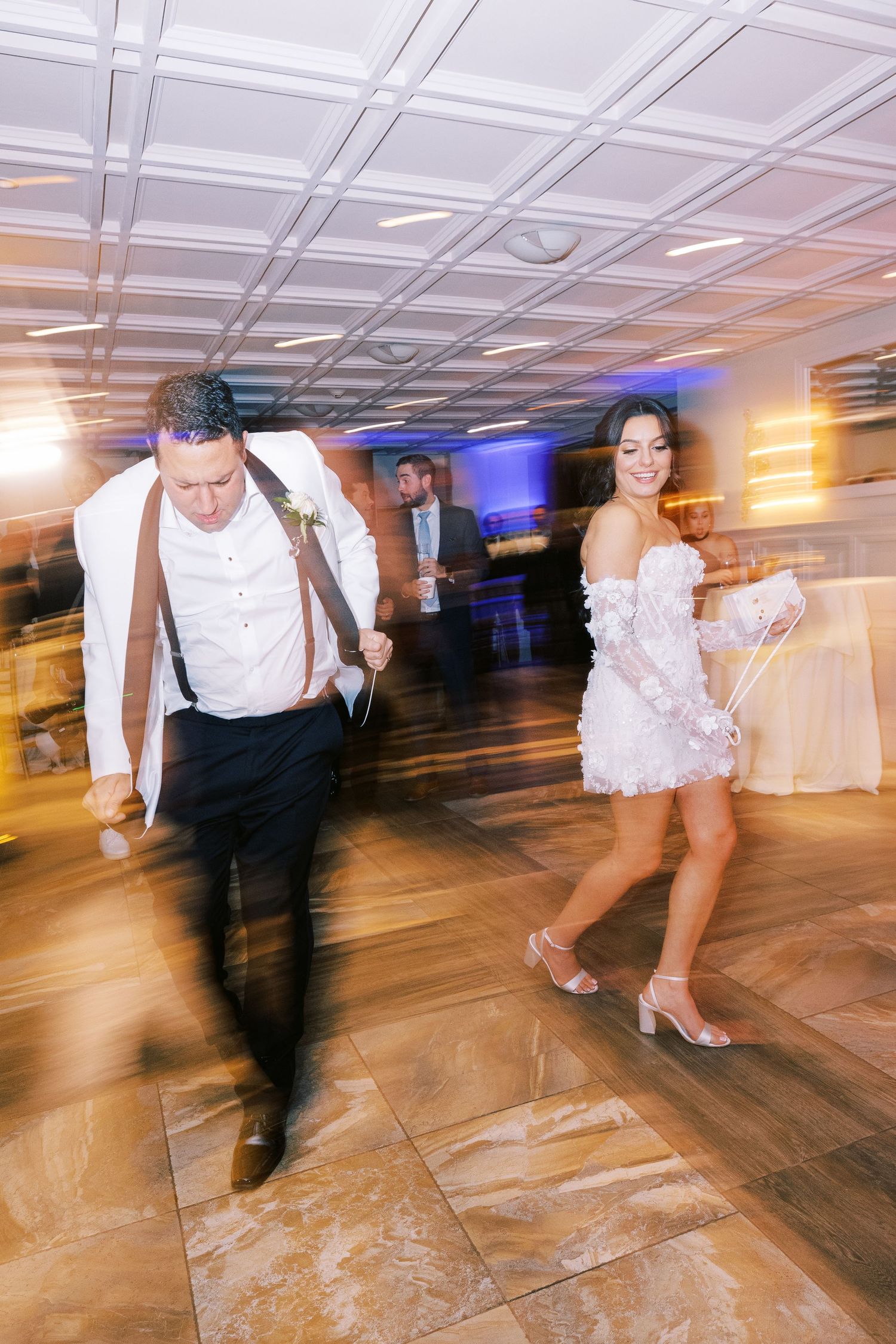 Bride in short white dress and groom dance energetically at lively wedding reception party.