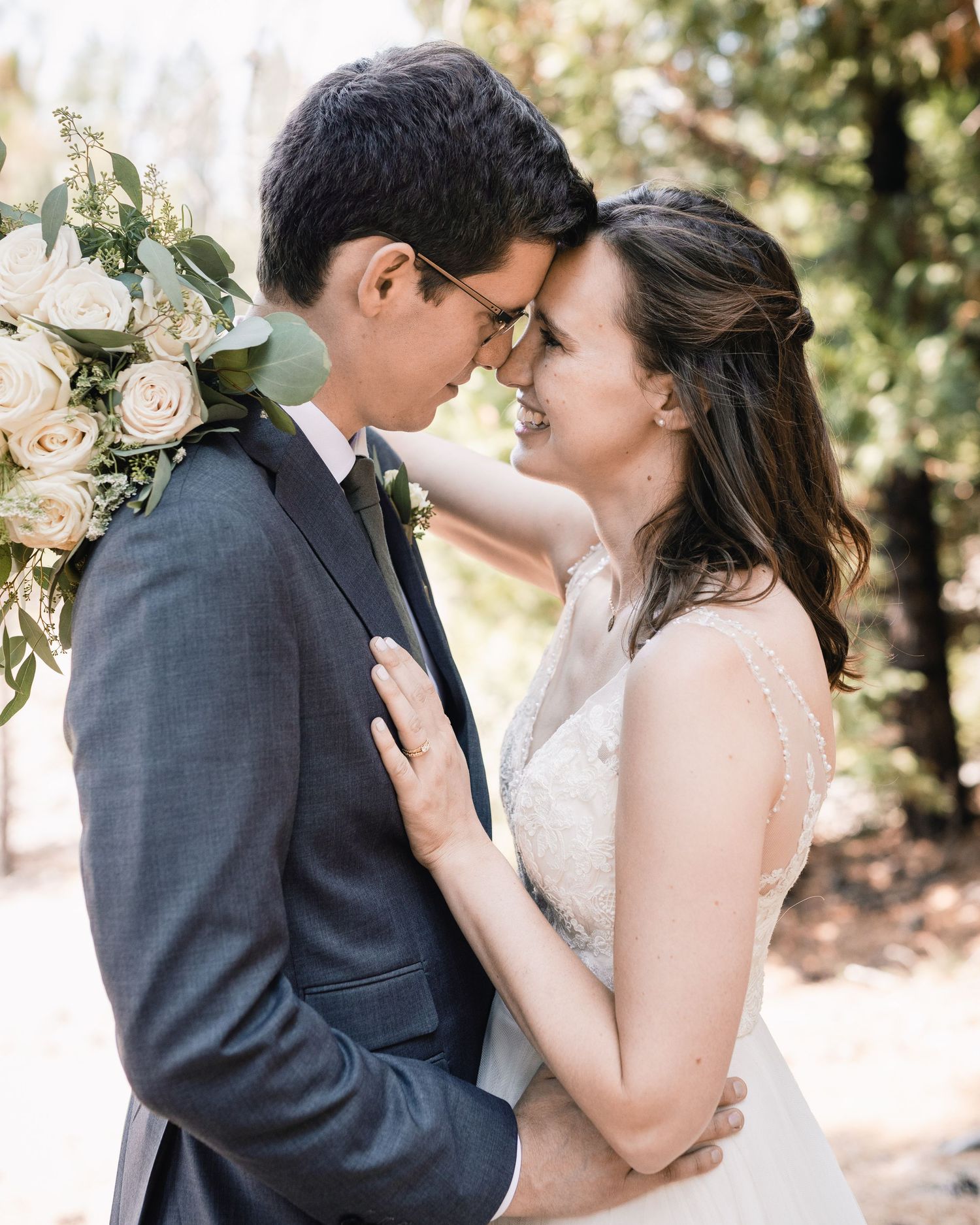 A romantic wedding couple shares an intimate moment outdoors with soft lighting and white floral bouquet details.