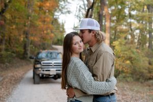 A romantic autumn photoshoot featuring a couple embracing on a dirt road with a pickup truck in the background.