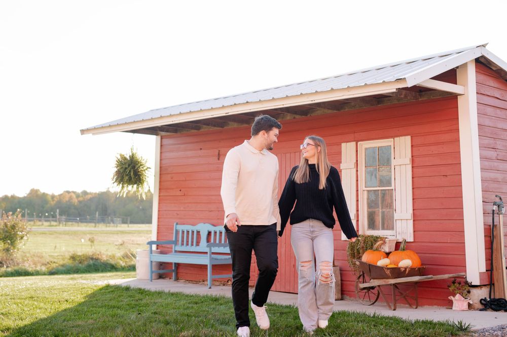 Couple walking together outside red cottage with blue bench and fall decorations.