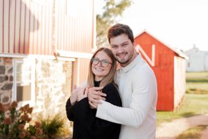 Happy couple embracing outside red barn in countryside setting.