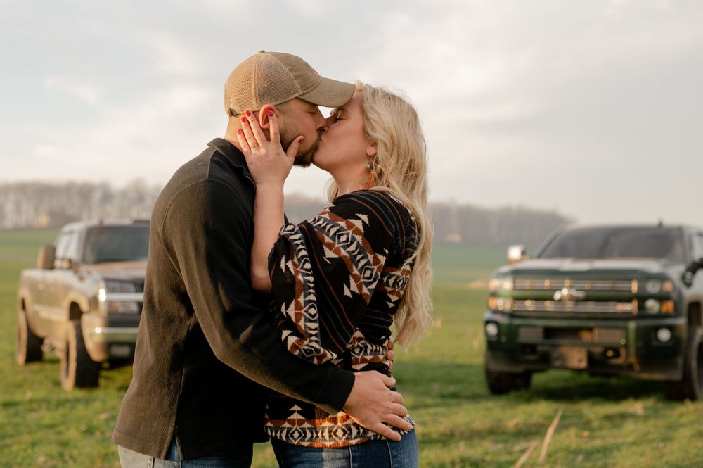 A romantic embrace between a couple in western attire with pickup trucks in the background.