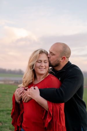 A tender embrace during sunset in a rural field with dramatic sky.