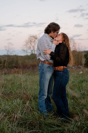 A romantic couple sharing an intimate kiss in a field at sunset wearing casual denim.