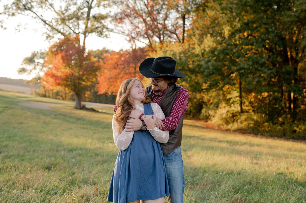 Couple in western attire embracing in a sunlit autumn field.