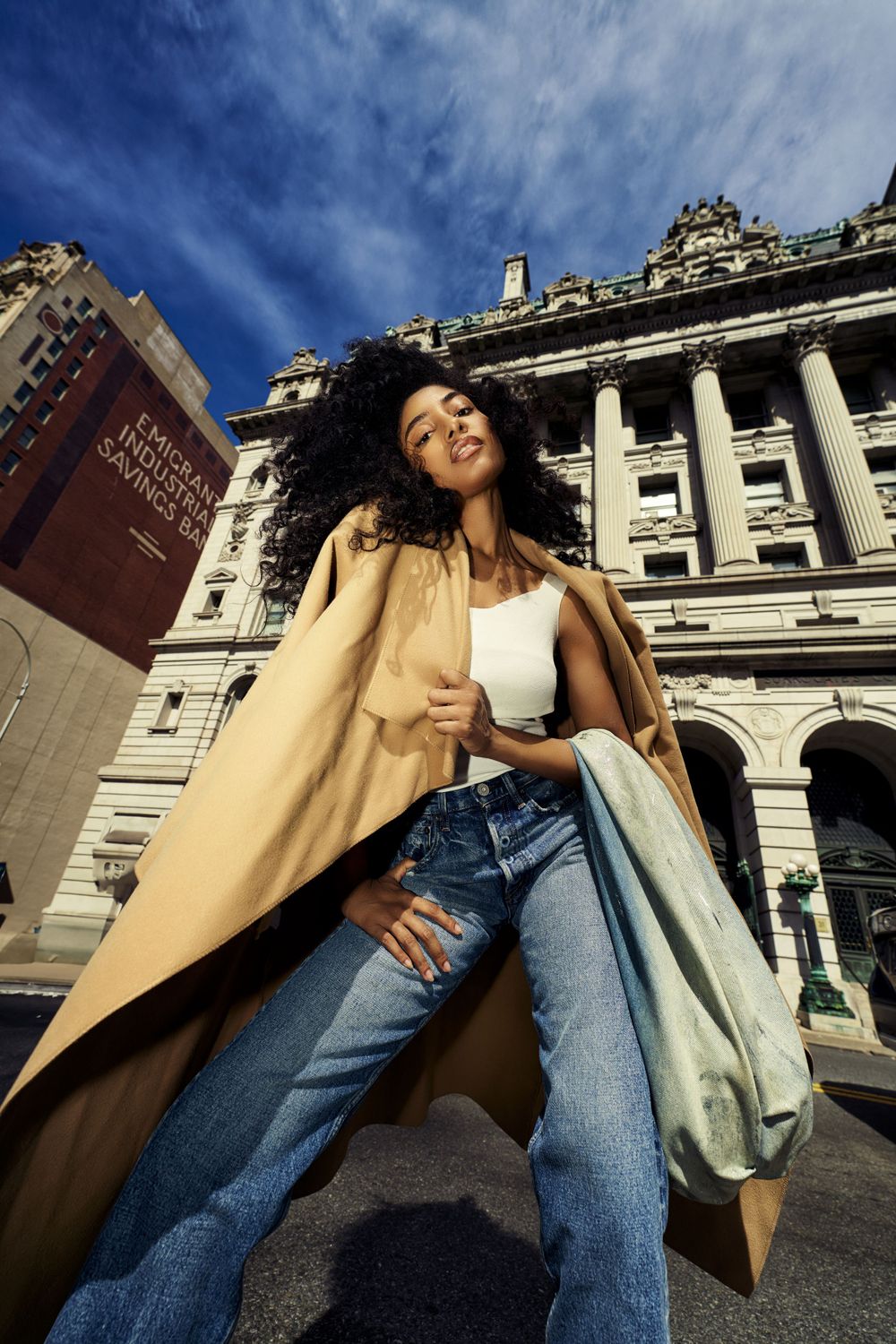Dynamic urban fashion sequence with tan coat and denim against classic architecture.