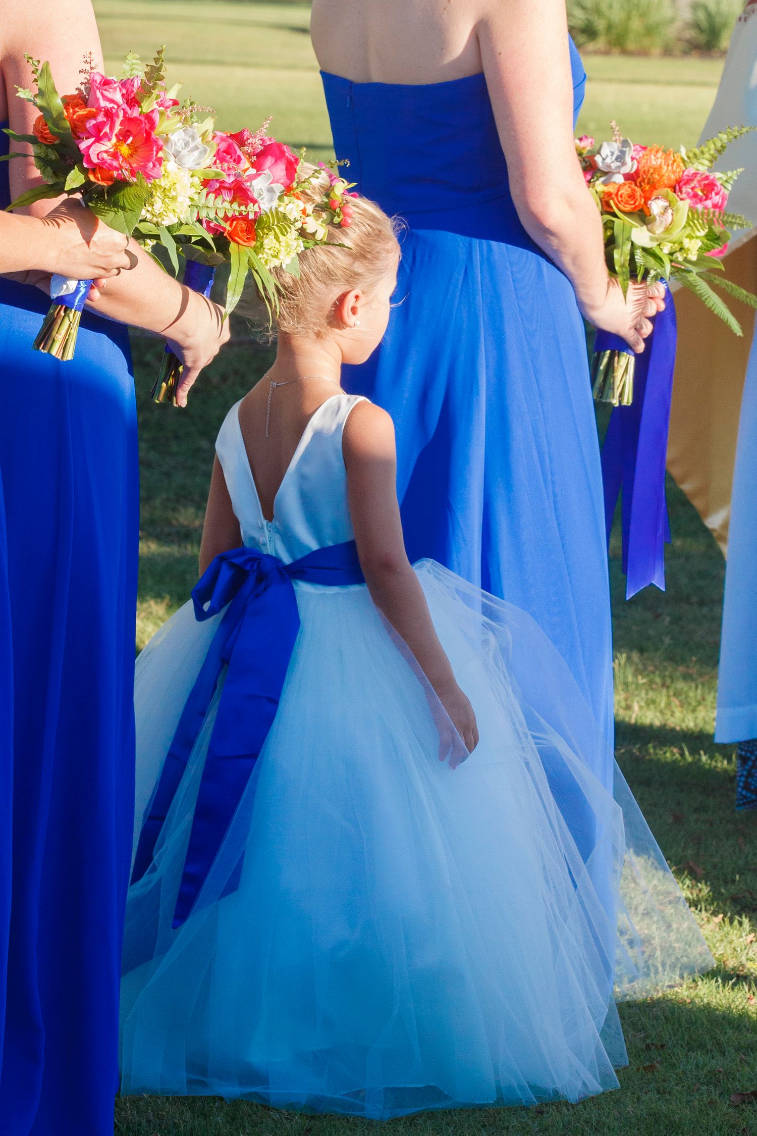 Flower girl in white and blue tulle dress standing with bridesmaids in royal blue gowns. Gasparilla Inn