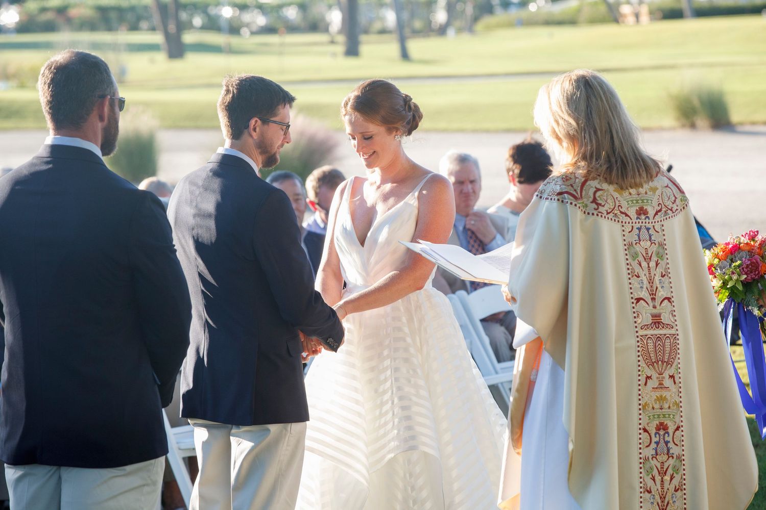Bride and groom exchange vows outdoors with officiant in ornate vestments at elegant wedding ceremony. Gasparilla Inn
