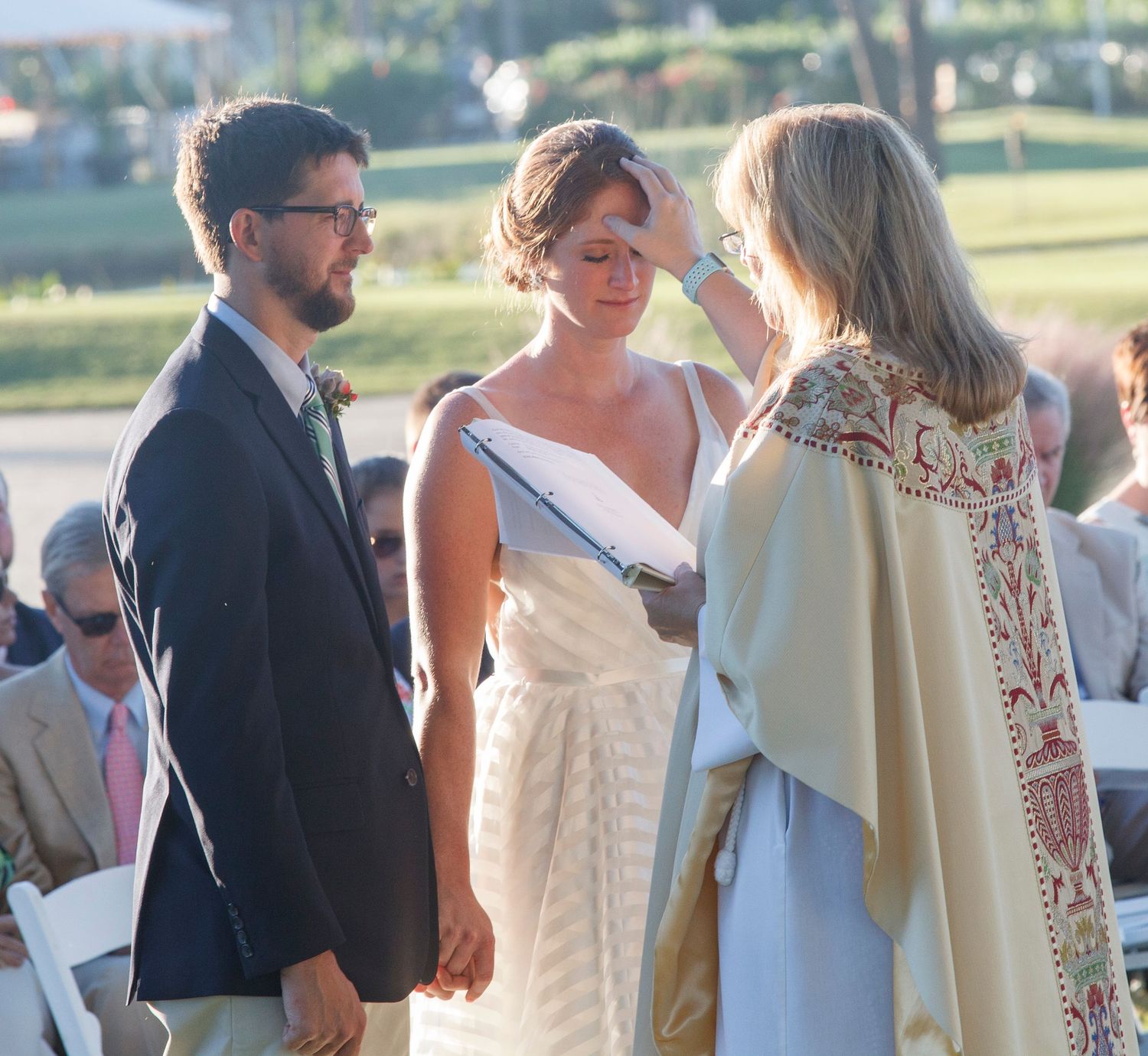 Wedding officiant in decorative vestments performs blessing on bride and groom during outdoor ceremony. Gasparilla Inn