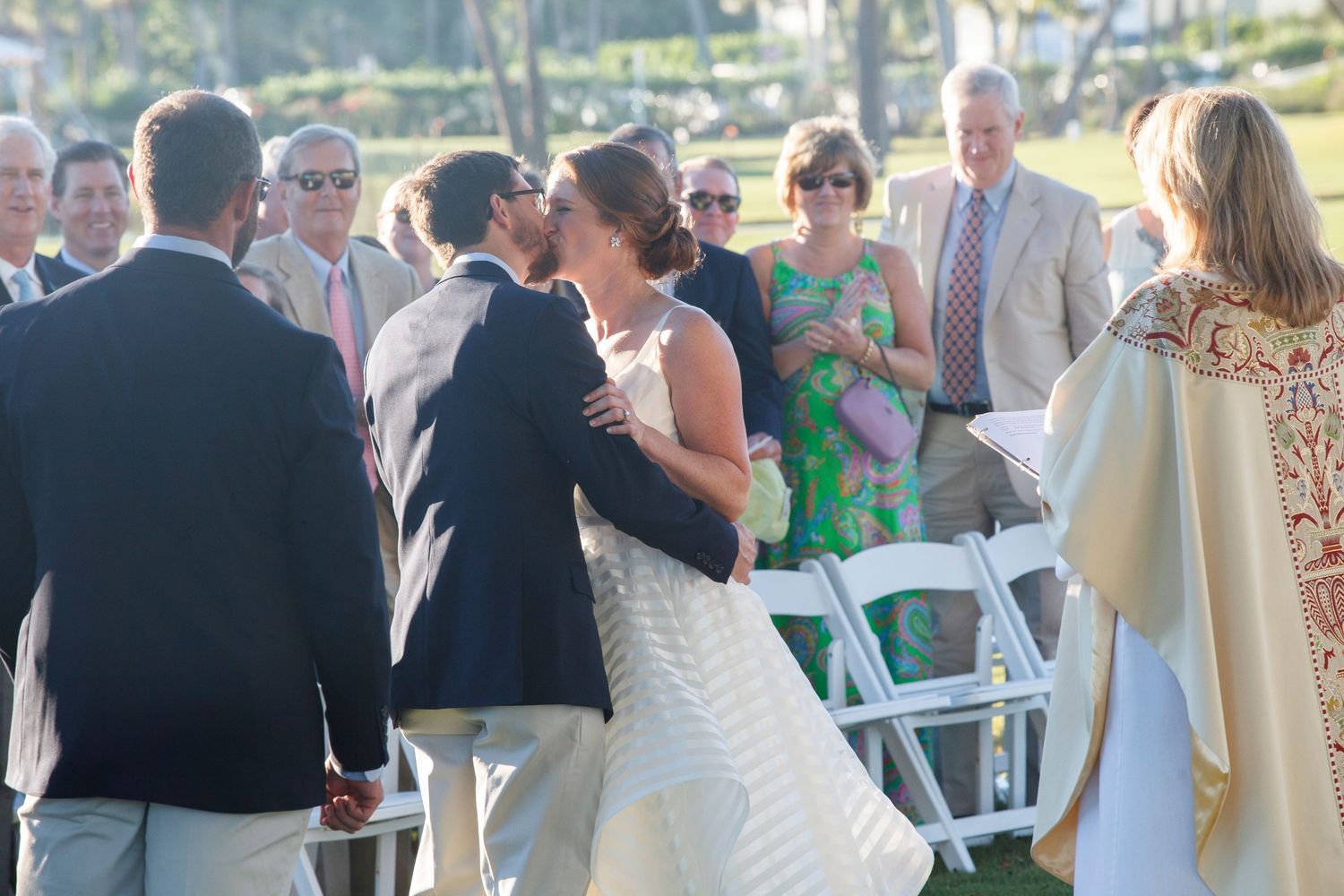 Bride and groom share first kiss at outdoor wedding ceremony with guests watching. Gasparilla Inn