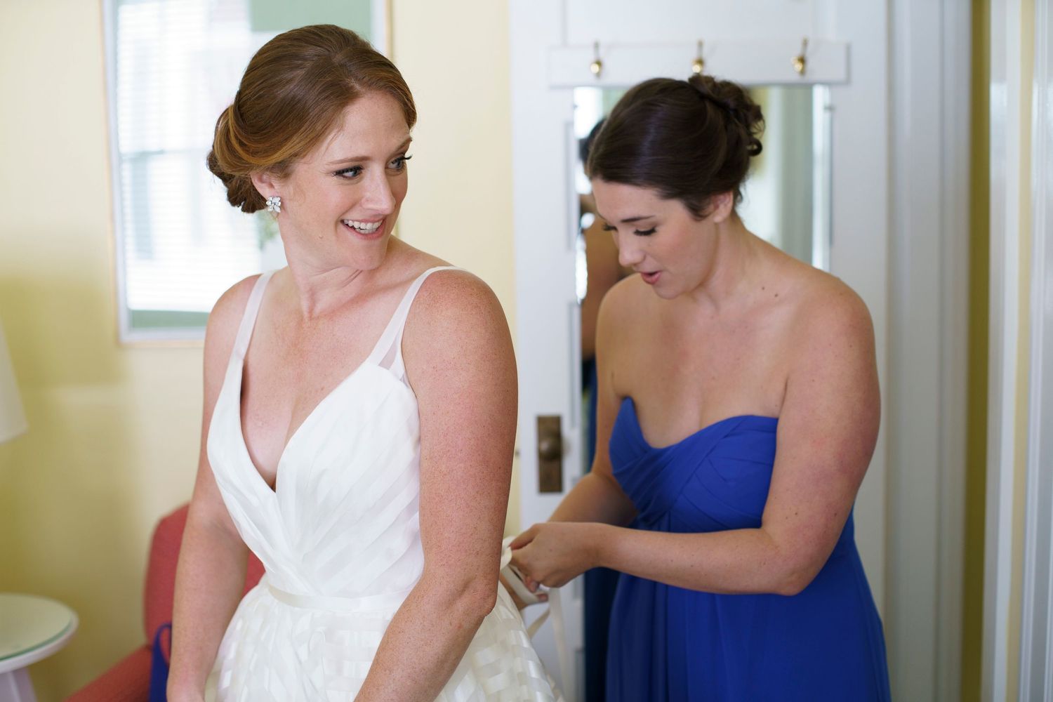 Bridesmaid in royal blue dress helps bride with wedding gown before ceremony. Gasparilla Inn