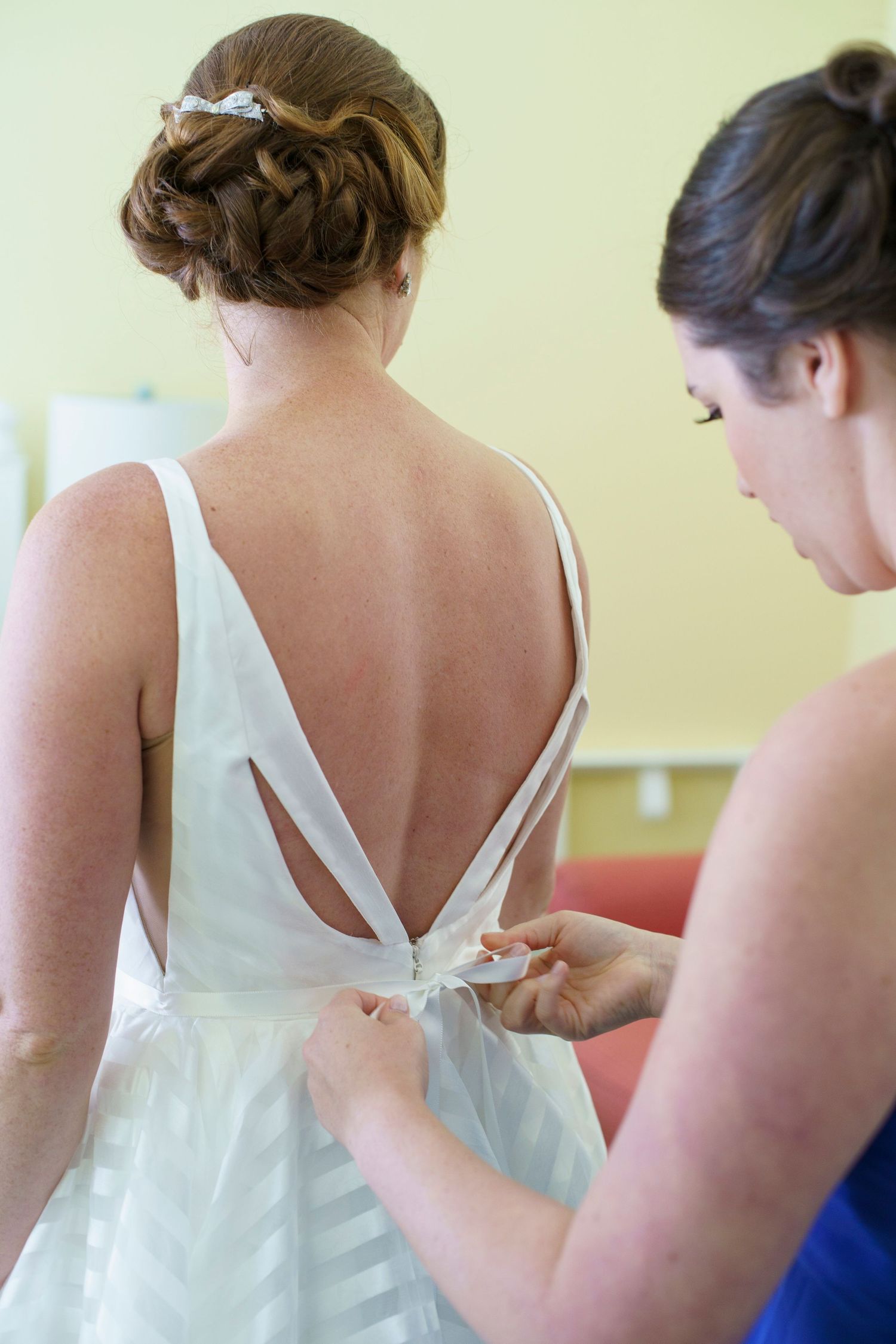 Bridesmaid fastening the back of bride's elegant low-back wedding dress. Gasparilla Inn