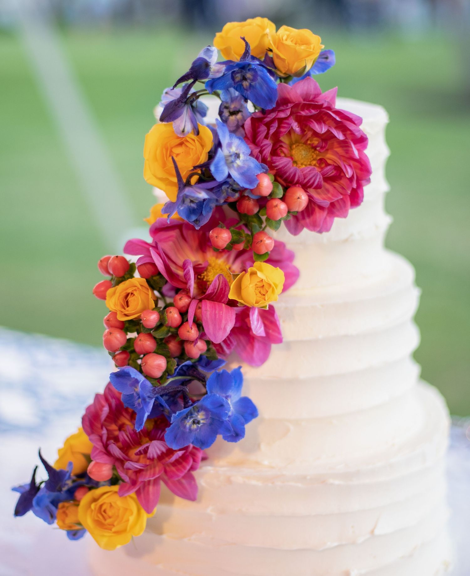 Three-tier white wedding cake adorned with cascading colorful fresh flowers. Gasparilla Inn