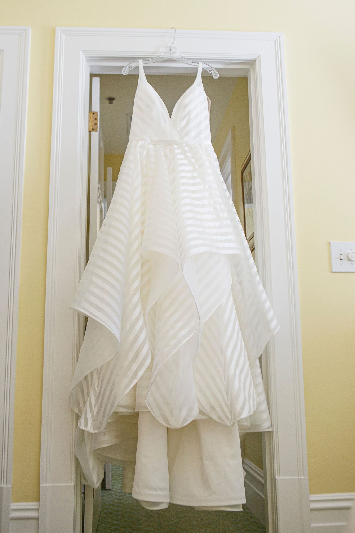 White striped layered wedding gown hanging on doorframe in yellow-walled bridal suite. Gasparilla Inn