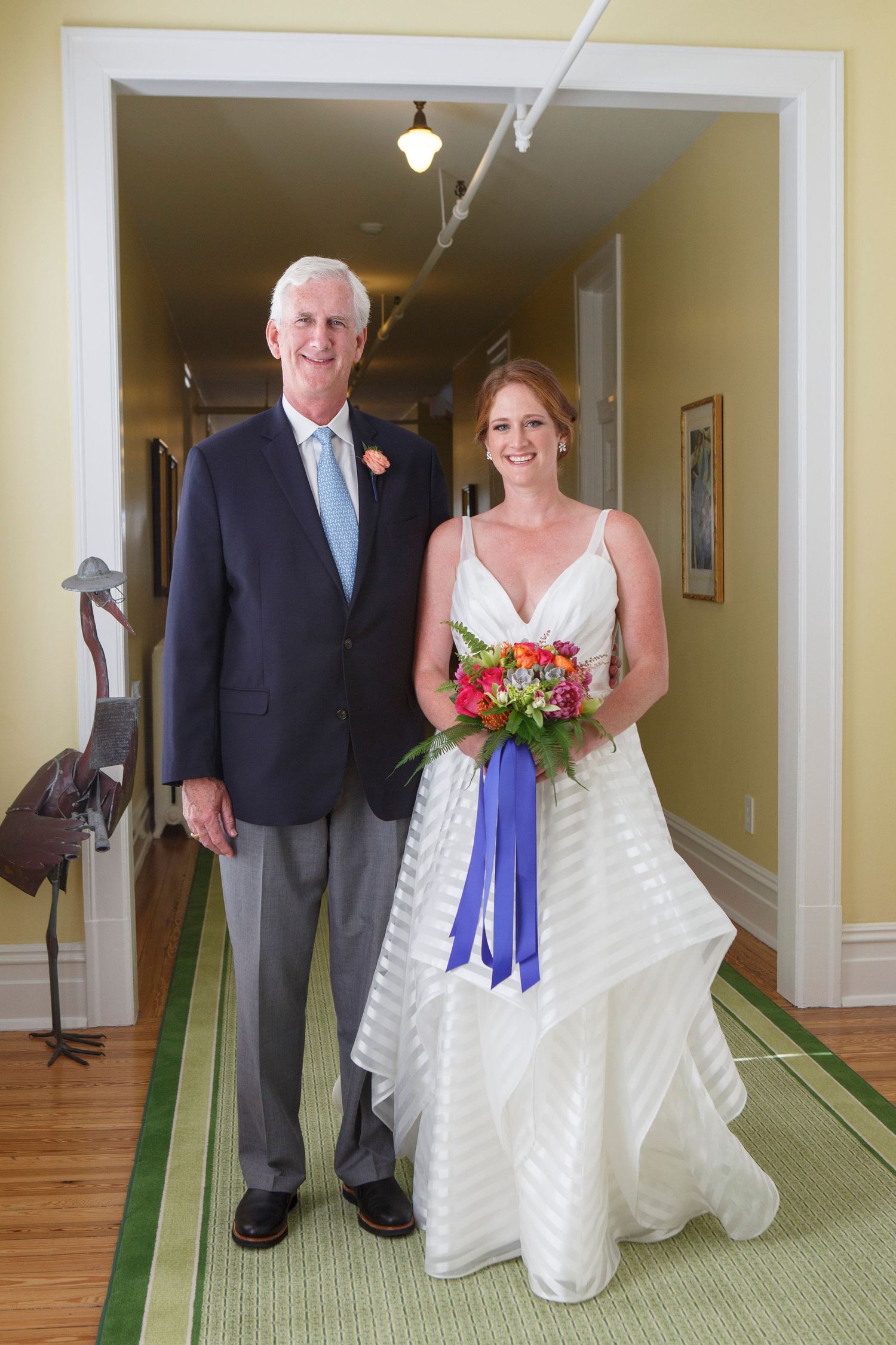 Bride holding colorful bouquet walks with father down hallway before ceremony. Gasparilla Inn