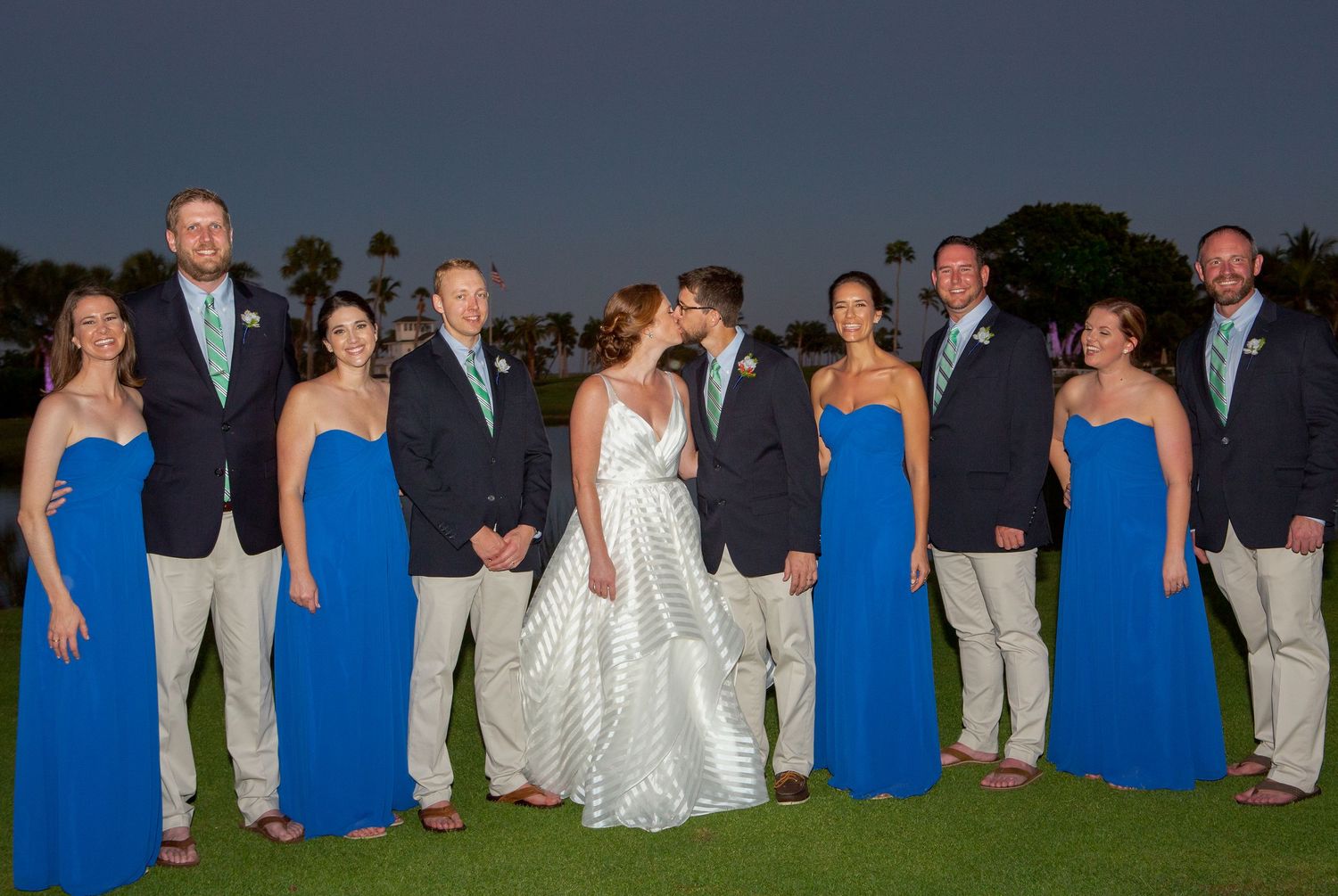 Wedding party poses at dusk on golf course, bridesmaids in blue, groomsmen in navy. Gasparilla Inn