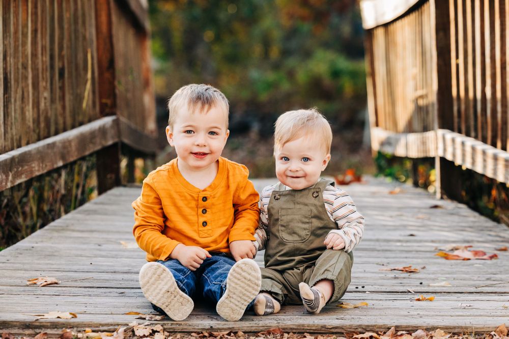Children sitting on wooden bridge surrounded by fall foliage.