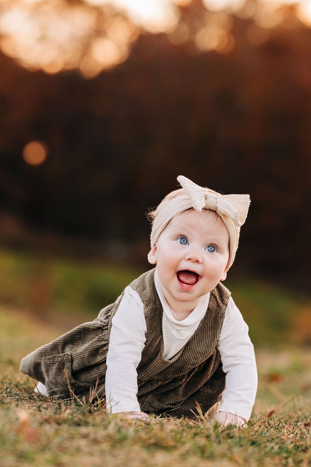 Baby in corduroy outfit crawling on grass during autumn photoshoot.