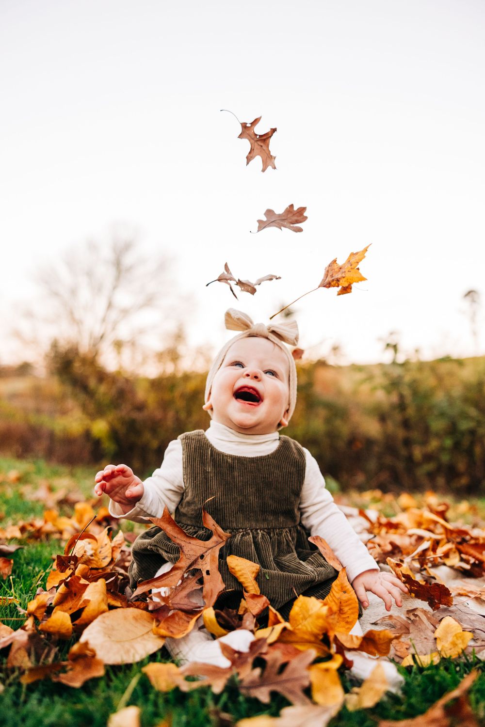 Baby playing with falling autumn leaves during outdoor photo session.