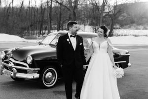 Black and white wedding image showing a couple next to a vintage 1950s car in winter.