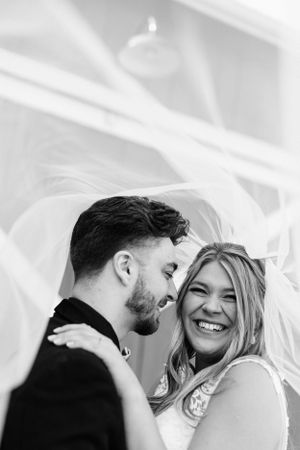 A tender black and white portrait of a couple sharing an intimate moment under a veil.