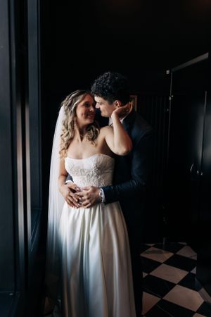 Romantic wedding couple embraces in moody lighting against black and white checkered floor.