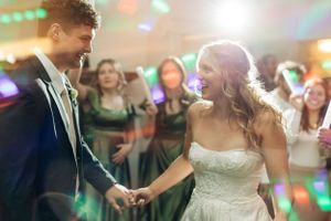 Couple shares their first dance at wedding reception with colorful disco lights and guests in background.