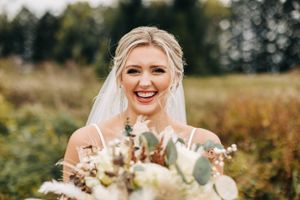 A joyful wedding portrait captured in a sunlit field with a delicate bouquet.