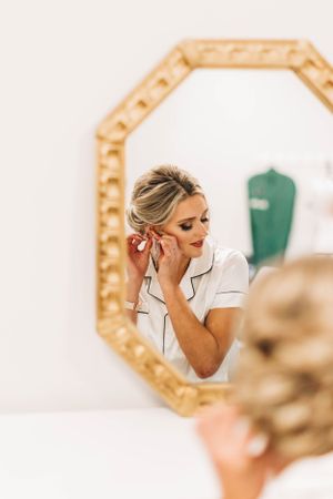 A reflection in a gold octagonal mirror shows someone putting on earrings while getting ready.