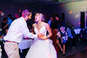 A couple dancing energetically at their wedding reception under colorful party lights.