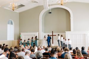 A wedding ceremony taking place in an elegant white chapel with arched architecture and chandeliers.