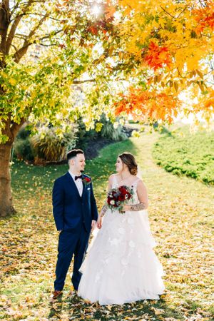 A couple standing among vibrant autumn foliage during their fall wedding photoshoot.