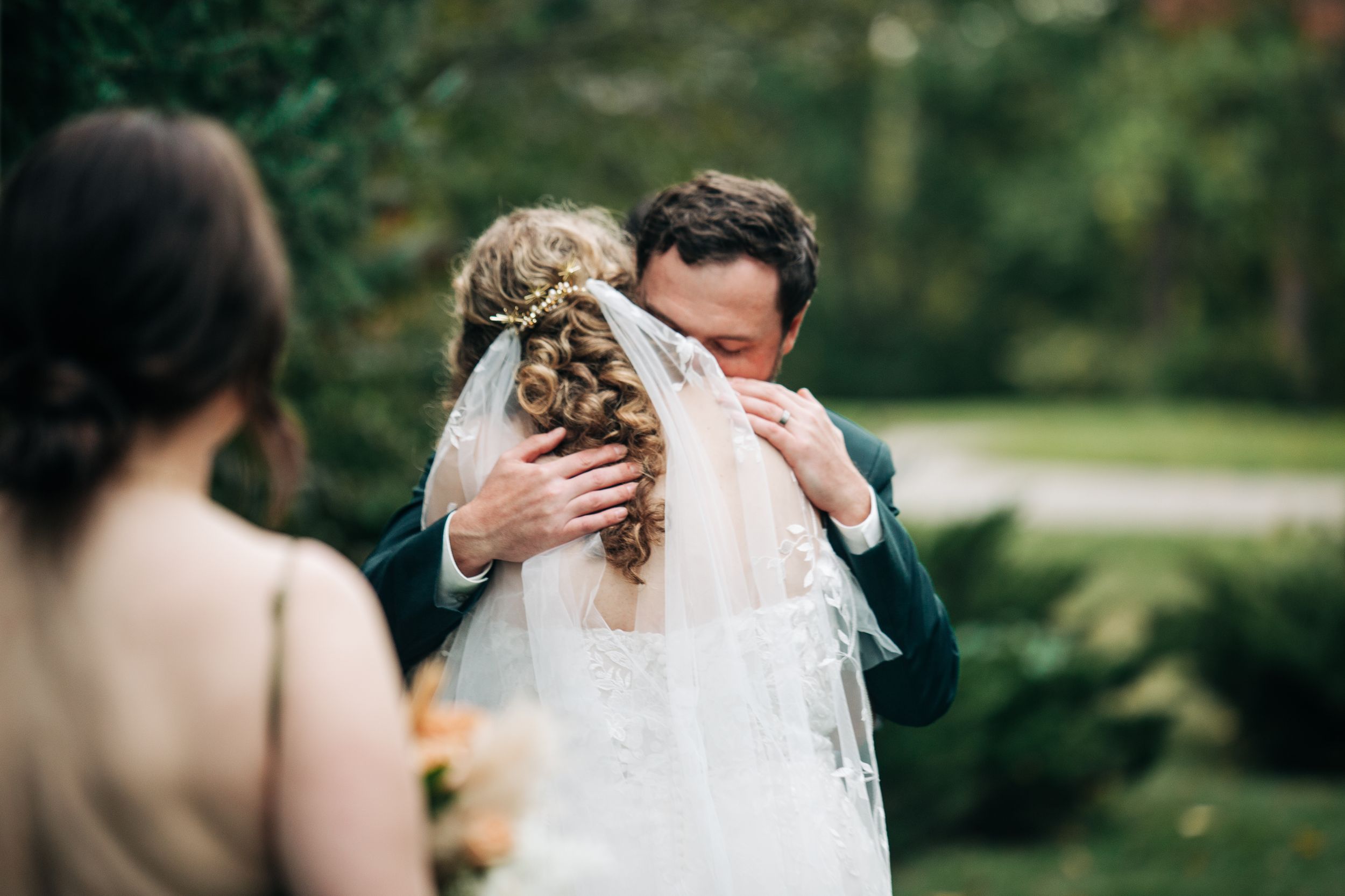 A tender embrace between newlyweds outdoors with the bride wearing a flowing white veil.