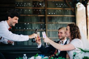 Wedding reception guests toasting with drinks at a rustic venue.