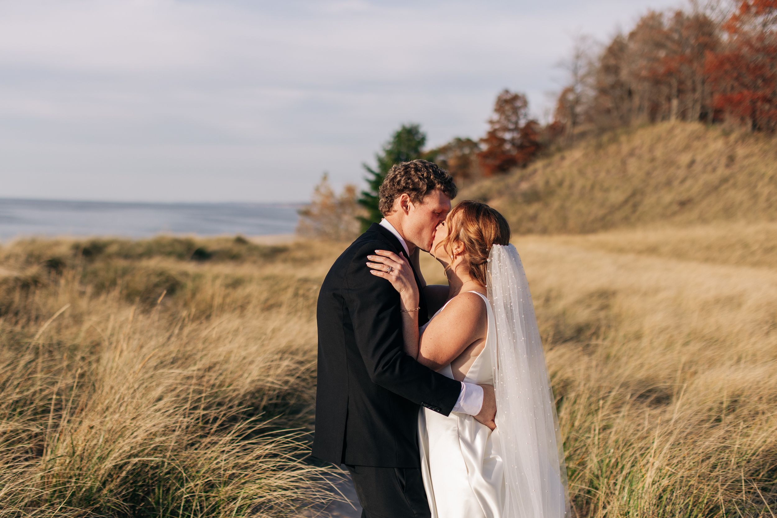 A couple shares an intimate moment on their wedding day along a coastal cliff.