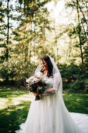 A wedding portrait showing a person in a white lace dress holding a luxurious burgundy and white bouquet.