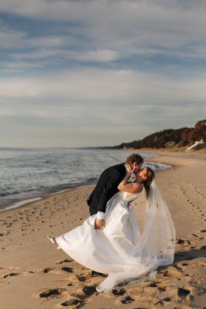 Couple sharing an intimate dip kiss on a scenic beach with cliffs and blue skies.