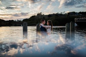 Romantic waterfront wedding photo at sunset with dreamy water reflections.